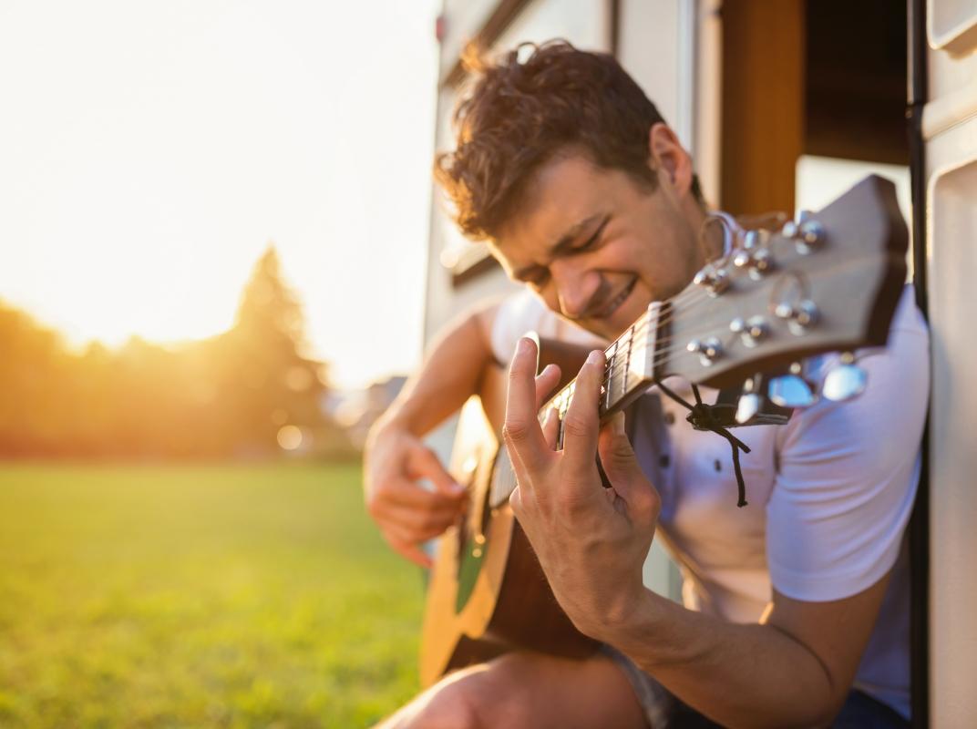 Mann mit Gitarre vor einem Campervan