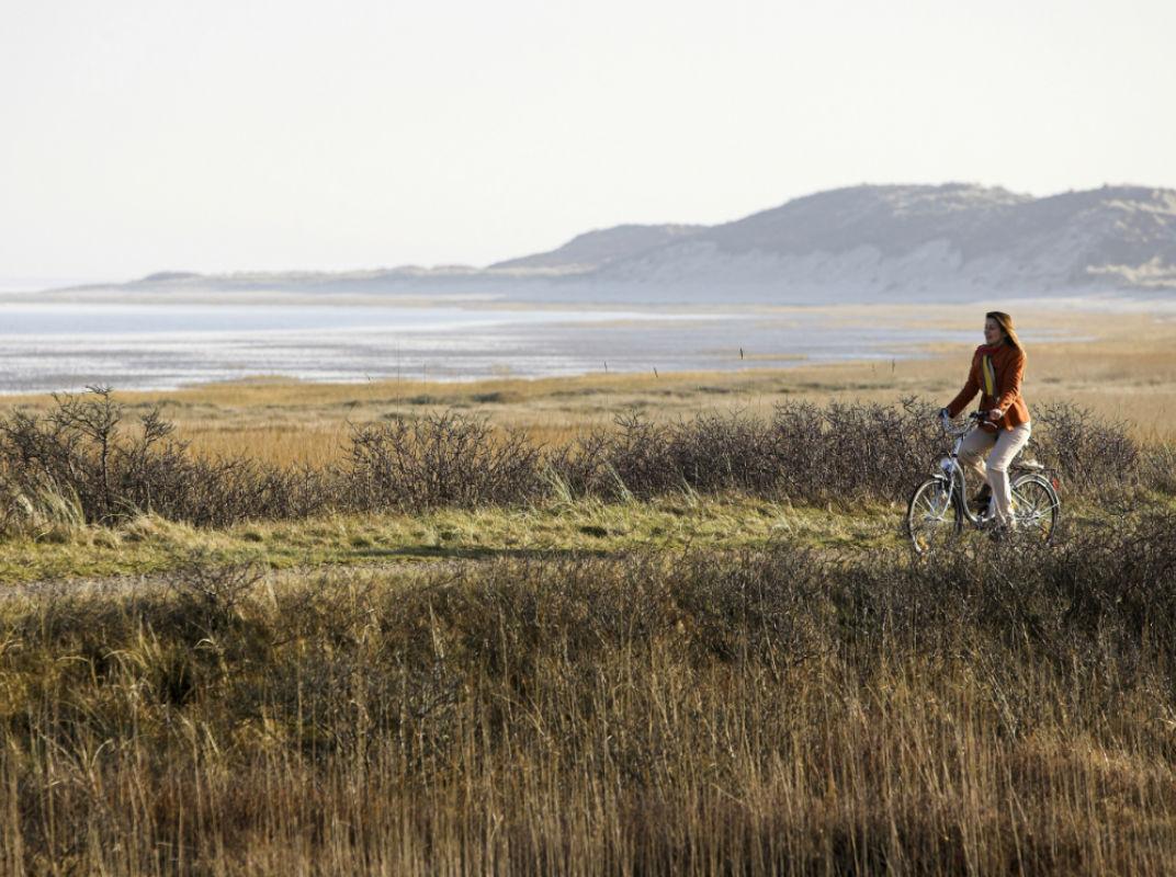 Frau fährt auf Fahrrad, im Hintergrund Strand und Hügel