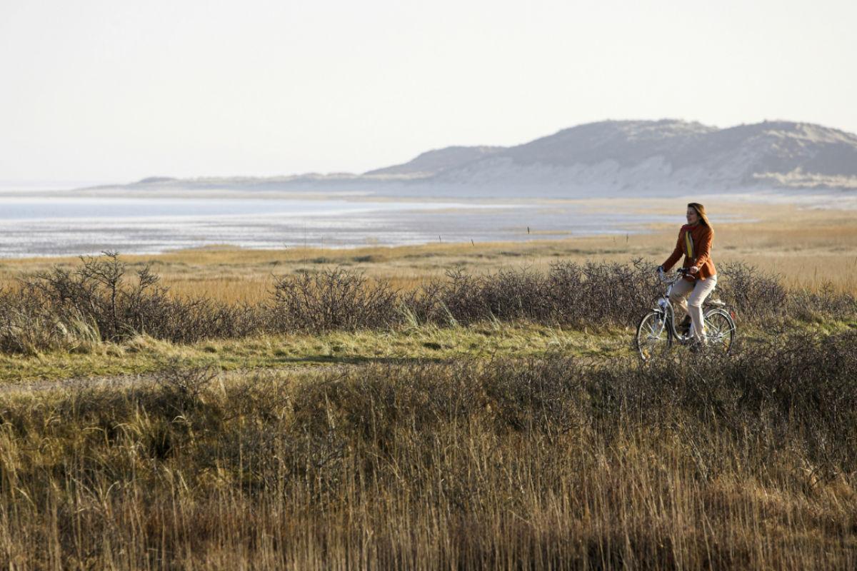 Frau fährt auf Fahrrad, im Hintergrund Strand und Hügel