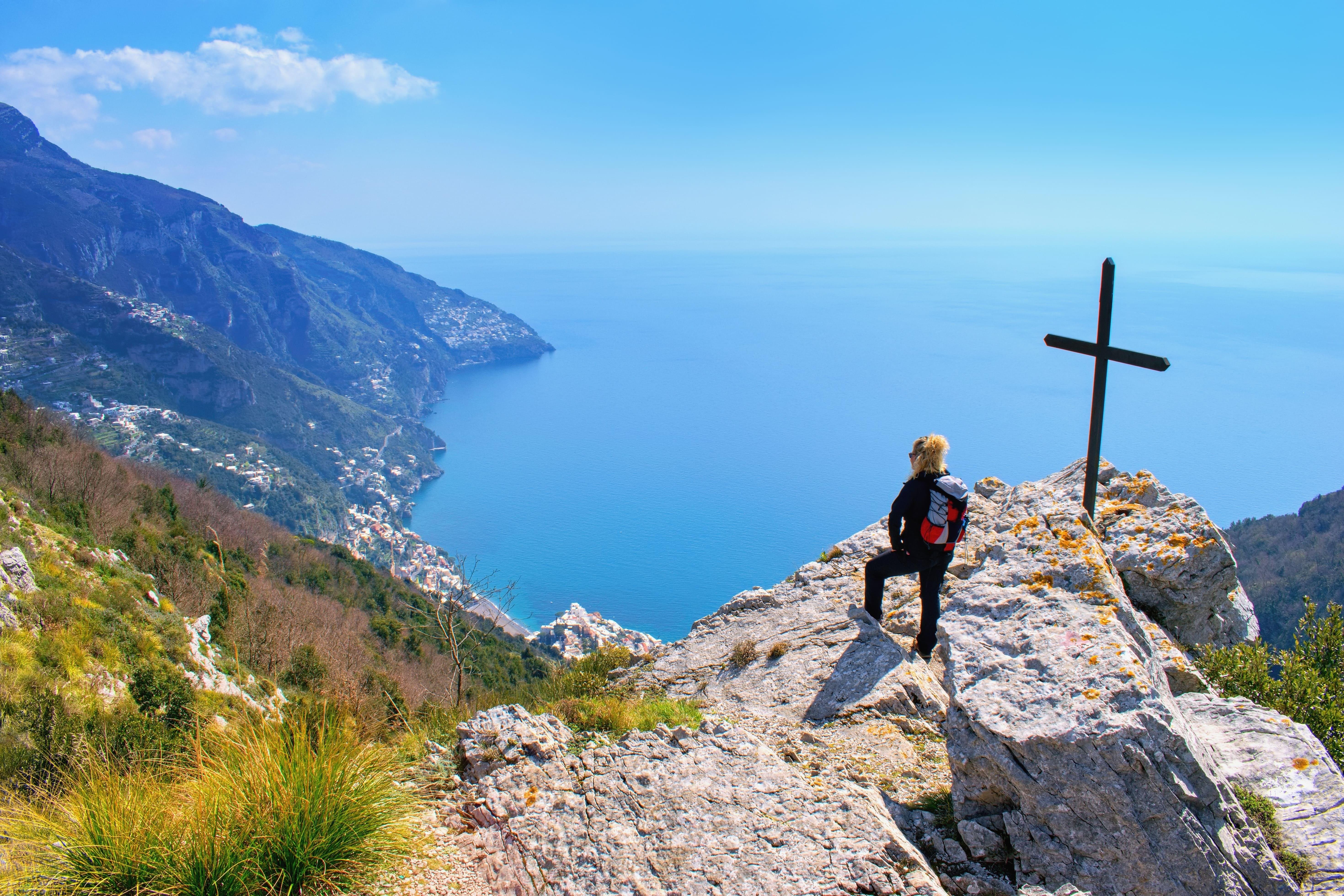 "Geschafft! Blick einer Wanderin vom Gipfelkreuz auf die Küstenszenerie."